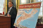 Communities, Culture and Heritage Minister Leonard Preyra talks about African Heritage Month beside this year's poster.