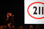 Service Nova Scotia and Municipal Relations Minister John MacDonell passes Chuck Hartlen, chair of the 211 Nova Scotia board, with the 211 symbol on the screen.