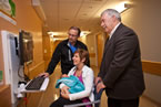 New father Chris Richard and Service Nova Scotia and Municipal Relations Minister John MacDonell stand behind Heather Richard with daughter Neaven, at one of the new bundled birth kiosks.