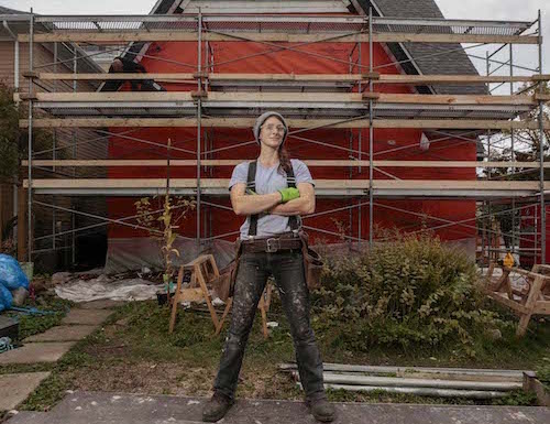Female construction worker posing in front of house with scaffolding