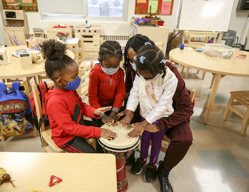 Female child worker teaching children to play the drum