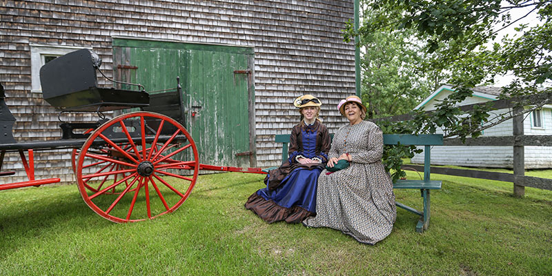 Two women wearing historical dress sitting on a bench next to a wagon