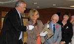  Director of Archives Management at Nova Scotia Archives Margaret Campbell looks through a newspaper from the time capsule as Communities, Culture and Heritage Minister David Wilson holds a microphone.