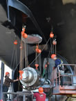 Workers lift part of a propeller into place.