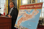Communities, Culture and Heritage Minister Leonard Preyra talks about African Heritage Month beside this year's poster.