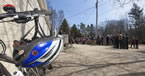 A helmet hands off handlebars as a group listens to the announcement in the background.