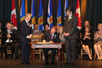 Energy and Communications Nova Scotia Minister Andrew Younger signs as Premier Stephen McNeil and Lt.-Gov. J.J. Grant look on.
