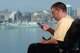 A silhouette of a man in a wheelchair checking his phone with Halifax harbour in the background.